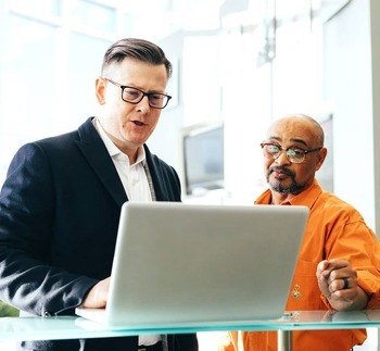 two men standing a desk looking at a computer